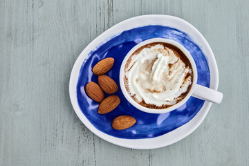 Cup of coffee with whipped cream, almonds on a blue wooden table