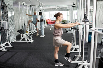 Side view portrait of smiling young woman doing rehabilitation exercises at gym in clinic, copy space