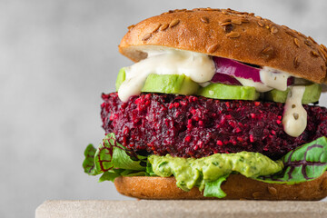 Close up of vegan burger with beet, avocado, mayonnaise, onion and salad on gray background