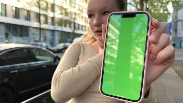 A teenage girl in a beige jacket holds a phone with chromatea and very satisfied shrugs her shoulders and smiles. High quality 4k footage