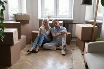 Sad tired elderly couple sit on floor near boxes with packed stuff feel exhausted due to long...