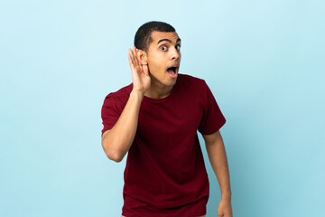 African American man over isolated background listening to something by putting hand on the ear