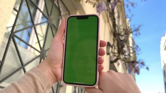 A woman's hand with vitiligo holds smartphone with green screen. Back view shot. Chroma key, close up woman hand holding phone with vertical green screen. High quality 4k footage