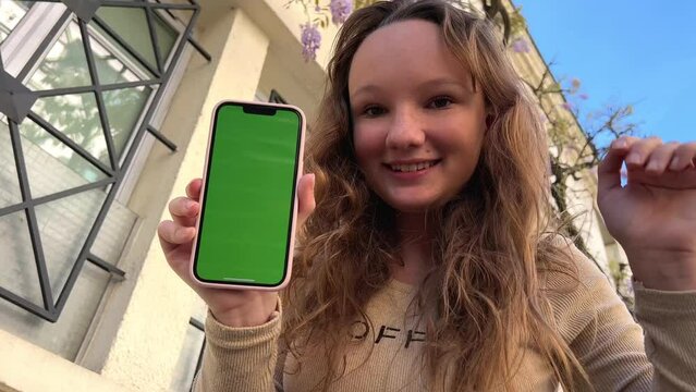 Teenage girl with loose hair brown hair brown hair dances with phone rejoices on the screen of lameness green screen beige background. High quality 4k footage