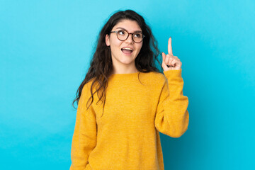 Teenager Russian girl isolated on blue background intending to realizes the solution while lifting a finger up