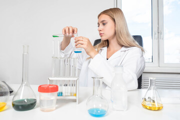 Chemistry blog. The study of chemistry. Girl demonstrates experiments. Woman mixes multicolored chemical liquids. Mixing of substances. Visual experiments. Girl at the table with chemical reagents