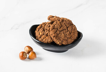 Cacao oatmeal cookies with hazelnuts in a serving bowl. White background	