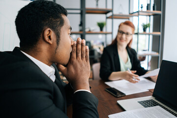 Stressed African-American businessman listening female team leader taking part at business meeting in conference room. Multi-ethnic business people listening female leader explaining project strategy.
