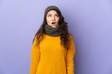 Teenager Russian girl with winter hat isolated on purple background looking up and with surprised expression