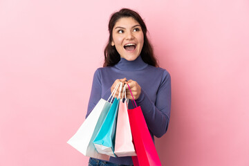 Teenager Russian girl isolated on pink background holding shopping bags and surprised