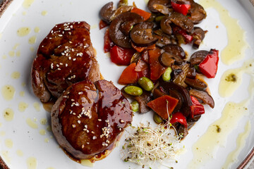 Grilled meat fillet steak wrapped in bacon medallions with raspberry sauce, served with vegetables and mushrooms