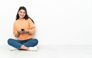 Teenager Russian girl sitting on the floor sending a message with the mobile