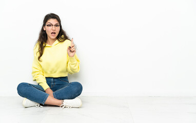 Teenager Russian girl sitting on the floor intending to realizes the solution while lifting a finger up