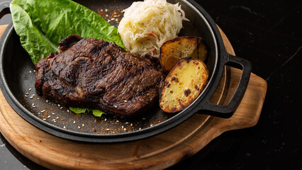Grilled steak with baked golden potatoes served with sour cabbage and red sauce on a dark background. Delicious Recipe. Pork Fillet Cooked on Skillet for Dinner . Fried Juicy Meat Texture.