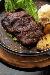 Grilled steak with baked golden potatoes served with sour cabbage and red sauce on a dark background. Delicious Recipe. Pork Fillet Cooked on Skillet for Dinner . Fried Juicy Meat Texture.