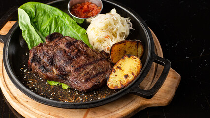 Grilled steak with baked golden potatoes served with sour cabbage and red sauce on a dark background. Delicious Recipe. Pork Fillet Cooked on Skillet for Dinner . Fried Juicy Meat Texture.