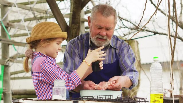 granddaughter helps grandfather cook barbecue and sprinkles the meat of pepper