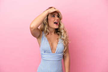 Young Brazilian woman in swimsuit in summer holidays isolated on pink background doing surprise gesture while looking to the side