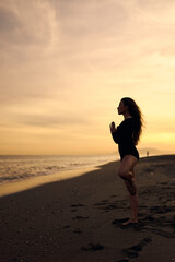 woman doing a yoga practice at the beach while a beautiful sunset