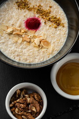 Semolina porridge for breakfast oat with nuts in black bowl served with honey isolated on black stone background. Homemade food. Tasty breakfast. Selective focus.