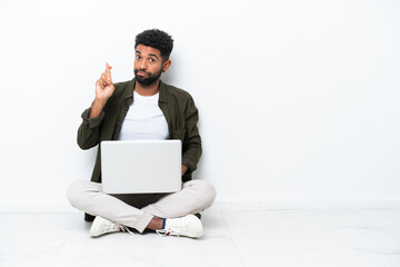 Young Brazilian man with a laptop sitting on the floor isolated on white with fingers crossing and wishing the best