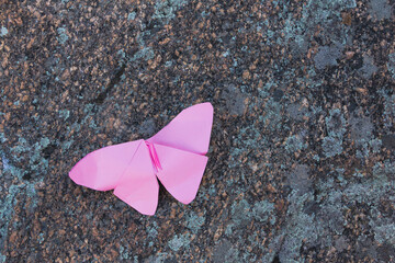 Pink paper butterfly on stone. Selective focus. Copy space.