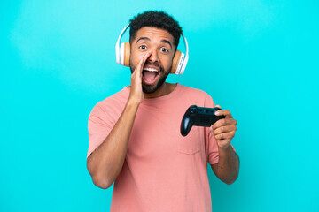 Fototapeta na wymiar Young brazilian man playing with a video game controller isolated on blue background shouting with mouth wide open