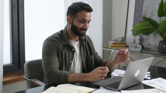 Pleasant friendly indian guy, manager or financial consultant, communicates with colleagues on a video call, discusses results and strategy, show financial graphs, remote negotiations, greeting
