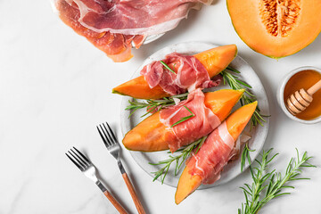 Italian antipasti. Melon cantaloupe slices with prosciutto ham, rosemary and honey in a plate on...