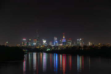 Night in big city of Warsaw skyline, high skyscrapers illumination reflected on Wisla river surface. Downtown beautiful cityscape panorama. Capital of Poland