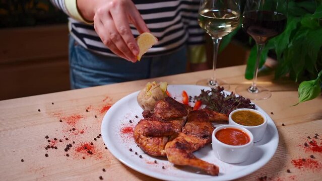 hand pouring lemon juice on roasted chicken tabaka on white plate in restaurant