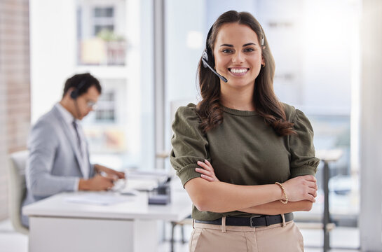 Delivering on excellent customer service. Portrait of a young call centre agent standing with her arms crossed in an office with her colleague in the background.