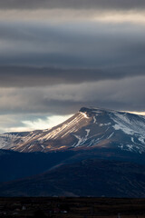Fototapeta premium colina y montañas con nieve, con nubes grises de lluvia y nieve, rayo de sol en atardecer