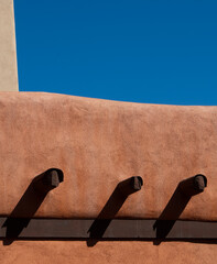 Obraz premium close up of adobe house against blue sky in Santa fe New Mexico with water run off drains abstract design of Santa Fe home architecture shapes and shadows while on holiday in Santa Fe vertical format