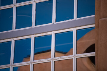 reflection in glass window of Santa Fe traditional adobe house design against blue sky close up pattern and shapes day time horizontal format design backdrop background or wallpaper showing  Santa Fe 