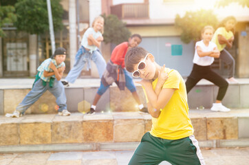Confident tween boy hip hop dancer posing while performing with group on summer city street.