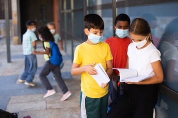 Portrait of three primary school children wearing face masks talking outside before lesson