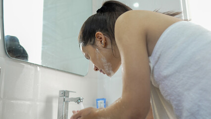 Young woman washing her face in the bathroom at home