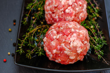  minced pork.meat balls close-up. Minced meat balls row with sprigs of thyme on a black plate on a...