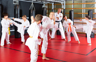 Diligent positive schoolchilds practicing kicks in pairs in karate class