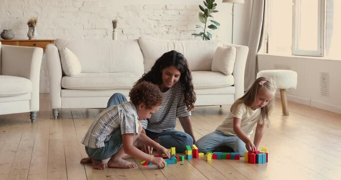 Hispanic female babysitter enjoy pastime with two kids siblings help children develop imagination in creative activity. Brother sister preschoolers construct buildings from toy blocks with caring mom