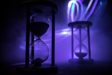 Time concept. Silhouette of Hourglass clock and old vintage wood clock with arrow and smoke on dark background with hot yellow orange red blue cold back lighting, or symbols of time with copy space
