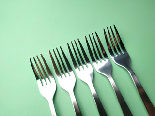 Stainless steel forks arranged on a green background.