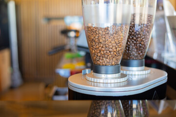 Close up shot with copy space of coffee beans in dispenser machine placing on table top in coffee shop with blur background of coffee preparation machine for background of beverage business.