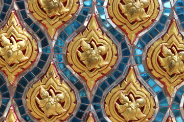 Traditional Thai stucco pattern decorated with golden flower and leaf on blue turquoise stained glass wall background in Thai temple. Original native Thai art. 