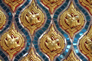 Fototapeta na wymiar Traditional Thai stucco pattern decorated with golden flower and leaf on blue turquoise stained glass wall background in Thai temple. Original native Thai art.