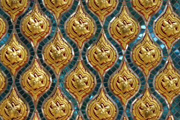 Fototapeta na wymiar Traditional Thai stucco pattern decorated with golden flower and leaf on blue turquoise stained glass wall background in Thai temple. Original native Thai art. 