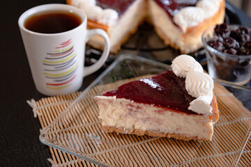 A slice  of cheesecake in a glass plate with a coffe cup  