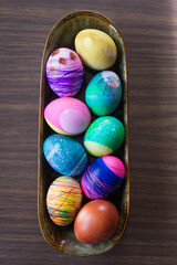 Hard boiled Easter eggs decorated by young children sit in a ceramic bowl on a wood table top; easy holiday DIY decor
