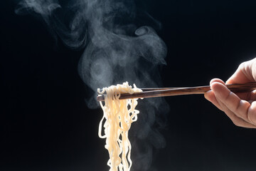wood chopsticks to pickup noodle with steam and smoke on black background. korea, japan, china,...